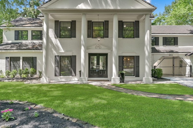 neoclassical / greek revival house featuring french doors, brick siding, a front lawn, and a gate