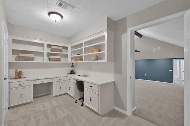 unfurnished office with light colored carpet, built in desk, a textured ceiling, baseboards, and vaulted ceiling