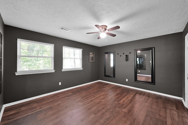 spare room with a textured ceiling, a ceiling fan, dark wood finished floors, healthy amount of natural light, and baseboards