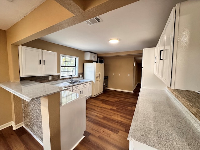 kitchen with white cabinetry, dark wood-type flooring, light stone counters, white refrigerator with ice dispenser, and kitchen peninsula