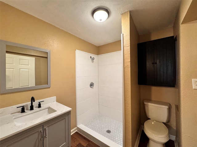 bathroom with a textured ceiling, vanity, tiled shower, hardwood / wood-style flooring, and toilet