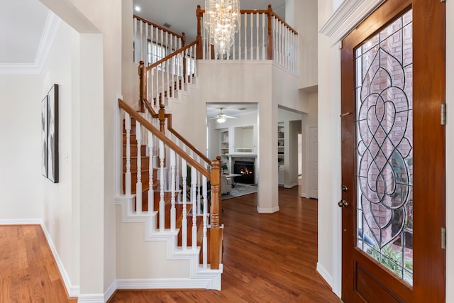 foyer entrance with a towering ceiling, wood-type flooring, ceiling fan with notable chandelier, and ornamental molding