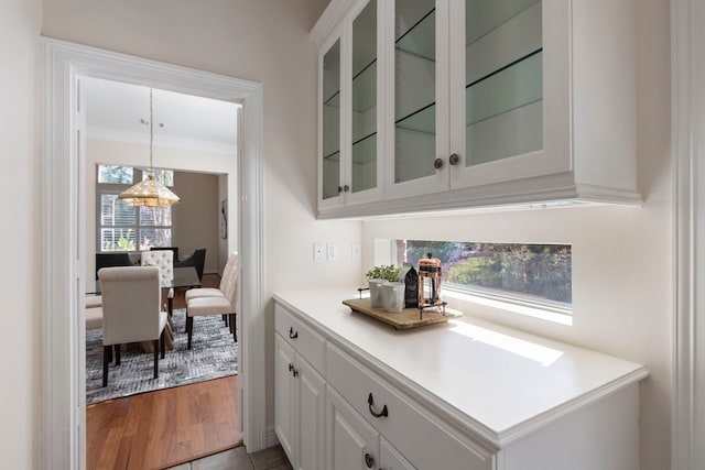 bar featuring white cabinetry, crown molding, light tile patterned floors, and hanging light fixtures