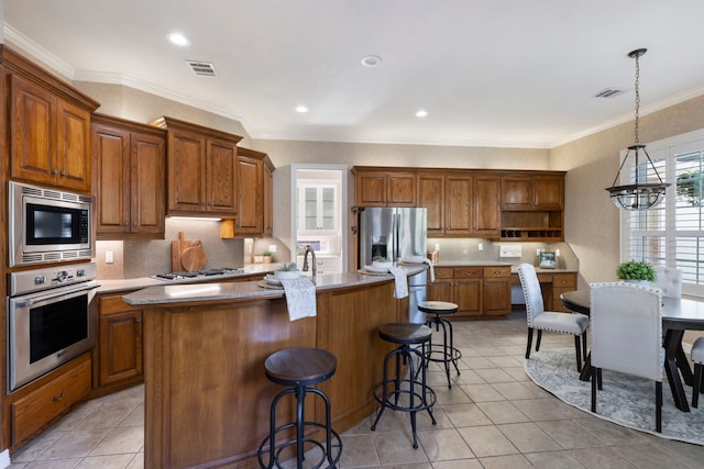 kitchen featuring stainless steel appliances, an inviting chandelier, decorative light fixtures, a center island with sink, and light tile patterned flooring