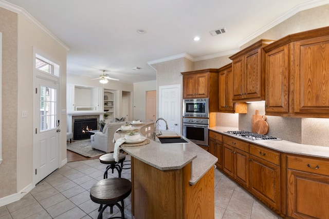 kitchen featuring a breakfast bar, sink, ornamental molding, an island with sink, and appliances with stainless steel finishes