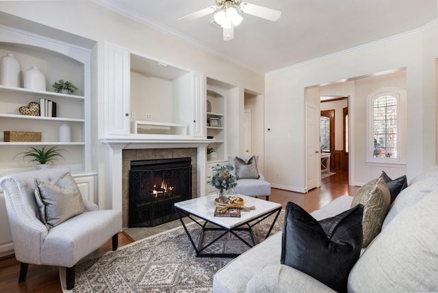 living room featuring a tile fireplace, built in shelves, light hardwood / wood-style floors, and ornamental molding