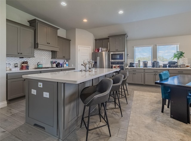 kitchen with a kitchen breakfast bar, gray cabinetry, a kitchen island with sink, and stainless steel appliances