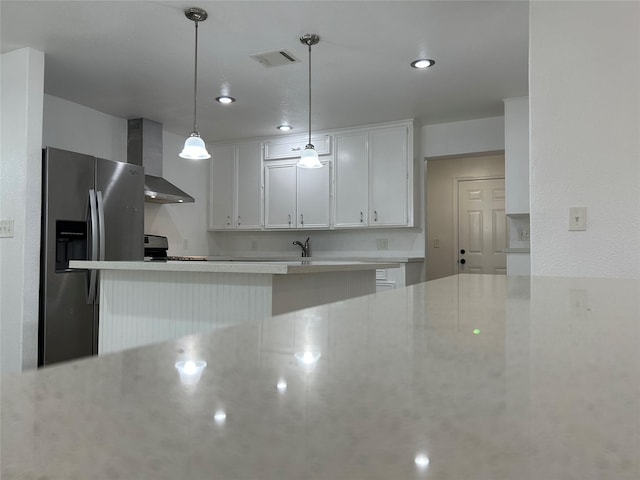 kitchen with range, wall chimney range hood, hanging light fixtures, stainless steel fridge, and white cabinetry