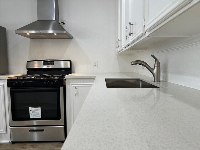 kitchen with white cabinets, gas stove, wall chimney range hood, and sink