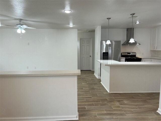 kitchen featuring appliances with stainless steel finishes, ceiling fan, wall chimney range hood, pendant lighting, and white cabinets