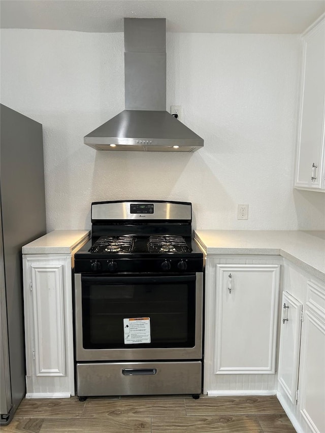 kitchen with white cabinets, appliances with stainless steel finishes, hardwood / wood-style flooring, and wall chimney range hood