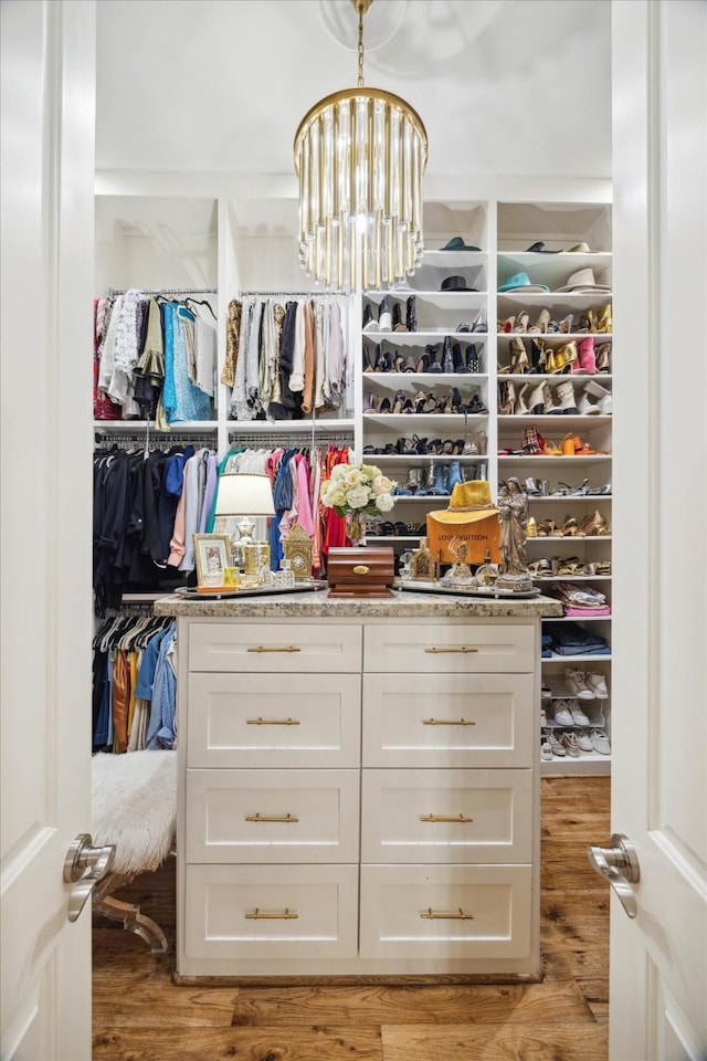 walk in closet with light hardwood / wood-style flooring and an inviting chandelier