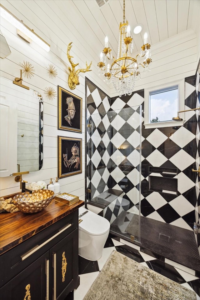 bathroom featuring a notable chandelier, tiled shower, wooden walls, toilet, and vanity