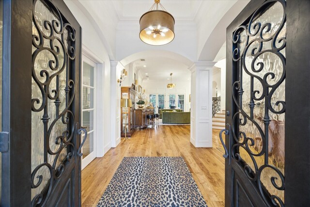 entryway featuring light wood-type flooring, decorative columns, and crown molding