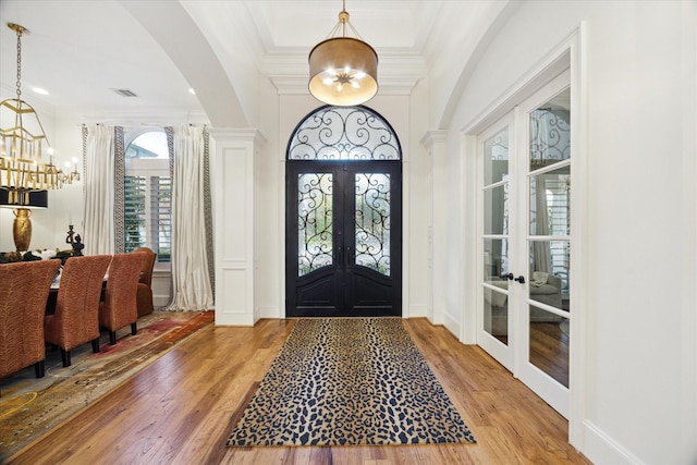 entrance foyer with french doors, a notable chandelier, crown molding, and hardwood / wood-style floors