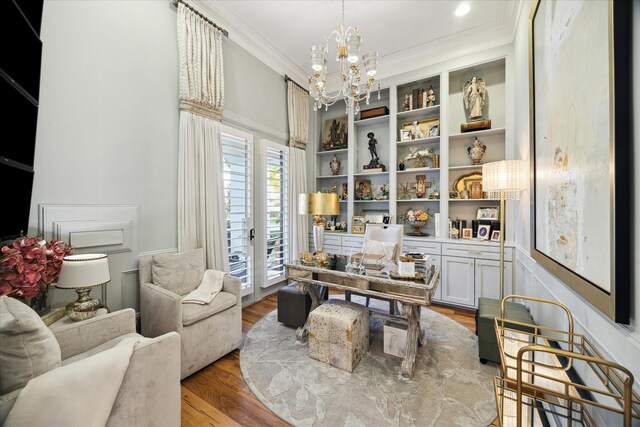 sitting room with built in shelves, light wood-type flooring, ornamental molding, and a chandelier