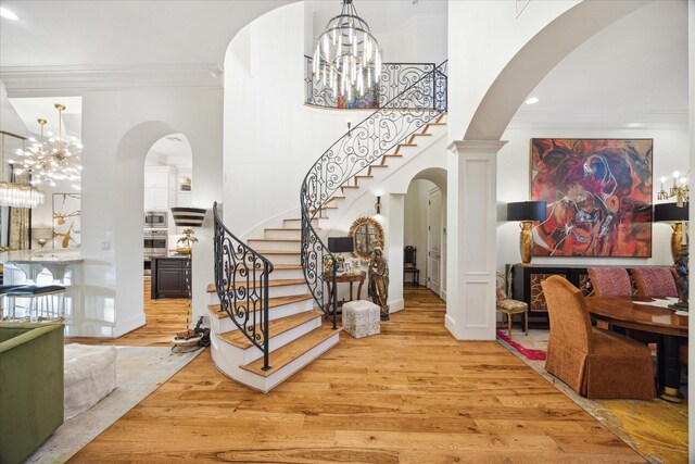 foyer featuring a notable chandelier, decorative columns, crown molding, and light hardwood / wood-style flooring