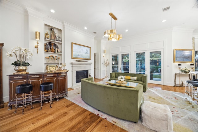 living room featuring built in shelves, french doors, light hardwood / wood-style flooring, a notable chandelier, and ornamental molding