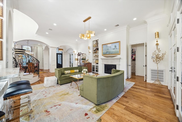 living room featuring a notable chandelier, light hardwood / wood-style floors, ornate columns, and built in shelves