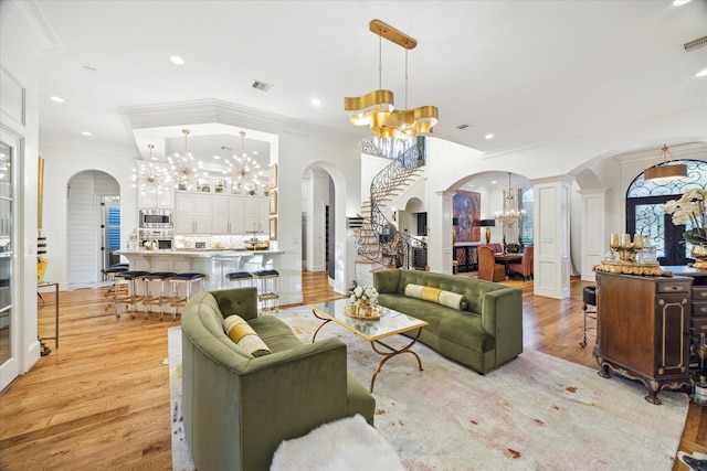 living room featuring a chandelier, decorative columns, light hardwood / wood-style flooring, and crown molding