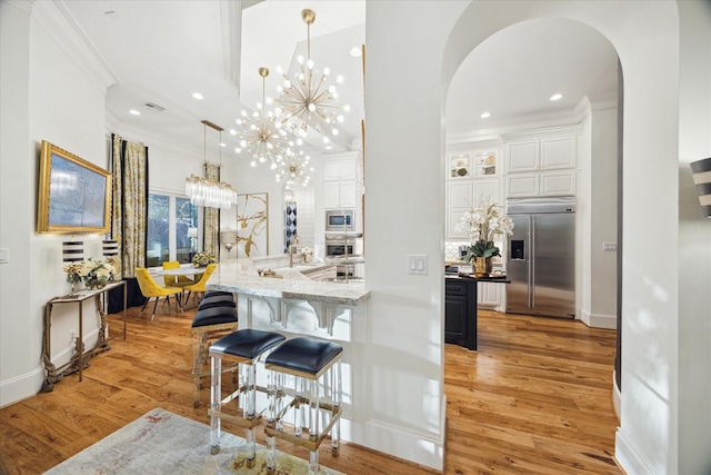 kitchen featuring an inviting chandelier, white cabinets, crown molding, built in appliances, and decorative light fixtures