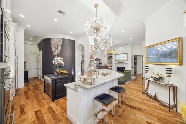 kitchen featuring a kitchen island with sink, a kitchen breakfast bar, oven, light hardwood / wood-style flooring, and light stone countertops