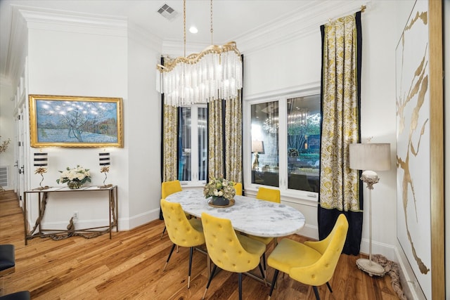 dining space with crown molding, hardwood / wood-style floors, and an inviting chandelier