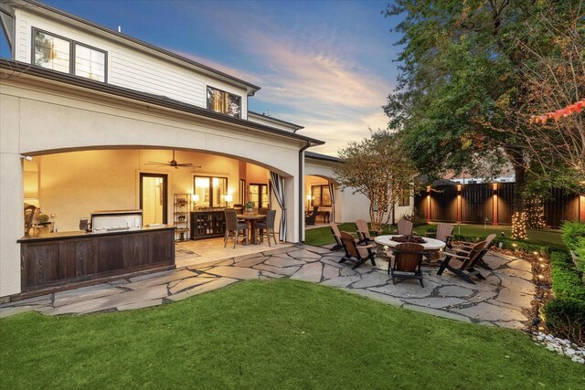 back house at dusk with a yard, a patio, a fire pit, and ceiling fan