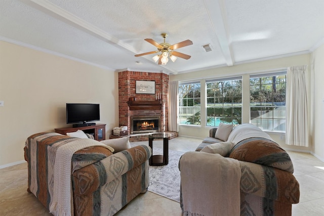 living room with beam ceiling, ceiling fan, a brick fireplace, a textured ceiling, and ornamental molding