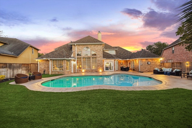 pool at dusk featuring an outdoor living space, a patio area, and a lawn