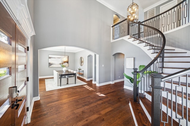 foyer entrance featuring an inviting chandelier, a towering ceiling, ornamental molding, and dark hardwood / wood-style flooring