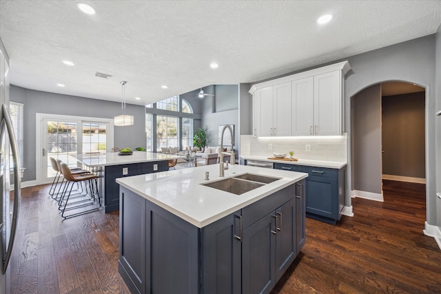 kitchen with pendant lighting, white cabinetry, an island with sink, sink, and a textured ceiling