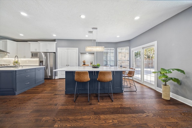 kitchen featuring stainless steel appliances, white cabinetry, dark wood-type flooring, and decorative light fixtures