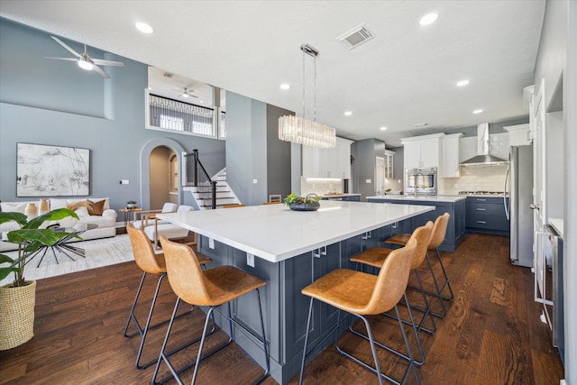 kitchen featuring blue cabinetry, wall chimney exhaust hood, a kitchen breakfast bar, pendant lighting, and white cabinets