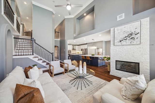 living room featuring crown molding, a towering ceiling, wood-type flooring, and a stone fireplace