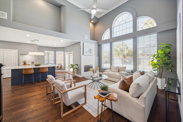 living room featuring a high ceiling, dark wood-type flooring, a large fireplace, and ceiling fan