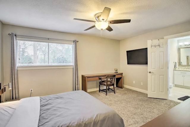 bedroom featuring ceiling fan, ensuite bathroom, a textured ceiling, and light carpet