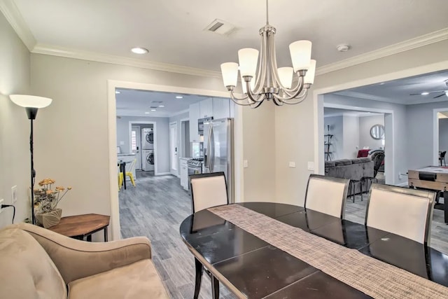 dining room featuring hardwood / wood-style floors, ceiling fan with notable chandelier, ornamental molding, and stacked washer / dryer