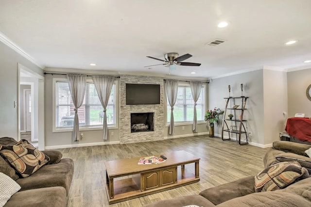 living room with light hardwood / wood-style flooring, ceiling fan, a stone fireplace, and crown molding