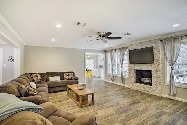 living room featuring crown molding, ceiling fan, a fireplace, and wood-type flooring