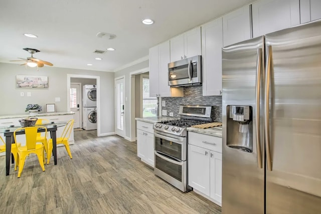 kitchen with backsplash, white cabinetry, stainless steel appliances, and stacked washer and clothes dryer