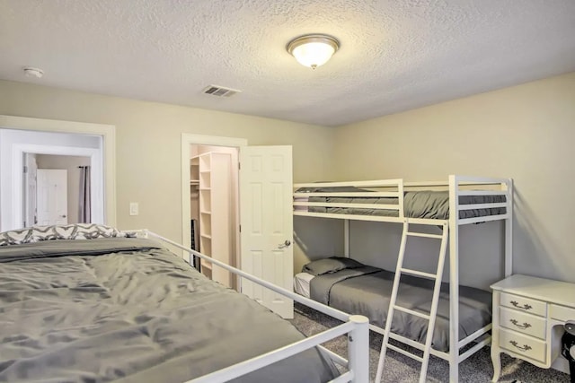 bedroom featuring a walk in closet, a closet, carpet floors, and a textured ceiling