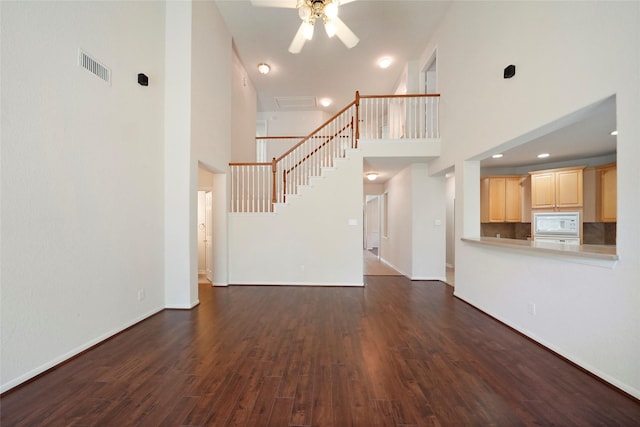 unfurnished living room with ceiling fan, dark hardwood / wood-style flooring, and a high ceiling