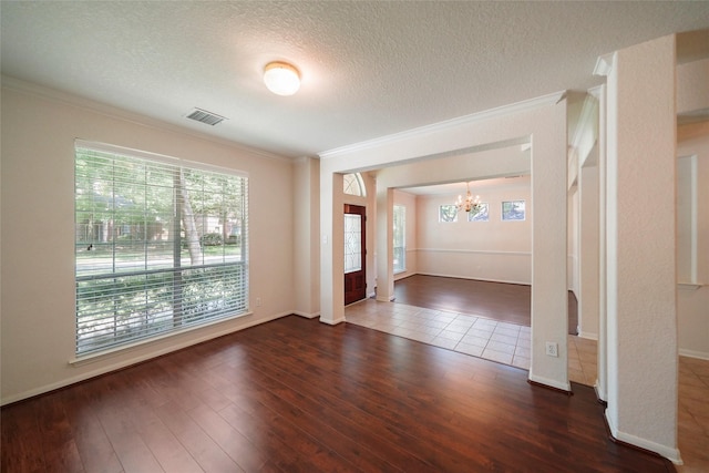 empty room with a textured ceiling, dark hardwood / wood-style flooring, crown molding, and a notable chandelier