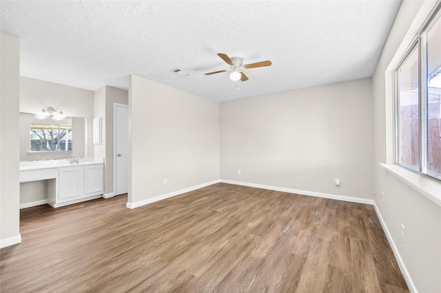 unfurnished bedroom with ceiling fan, sink, light hardwood / wood-style flooring, a textured ceiling, and built in desk