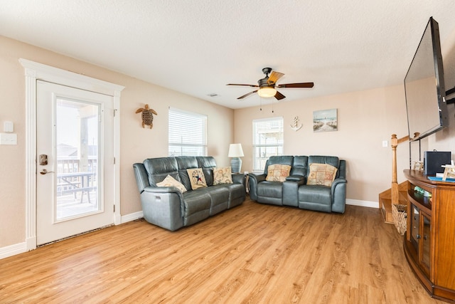 living room featuring ceiling fan, light hardwood / wood-style flooring, and a textured ceiling