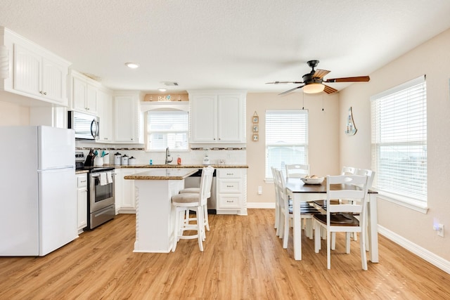 kitchen featuring white cabinets, appliances with stainless steel finishes, a center island, and decorative backsplash