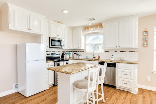 kitchen with white cabinets, light hardwood / wood-style floors, a kitchen island, light stone counters, and stainless steel appliances