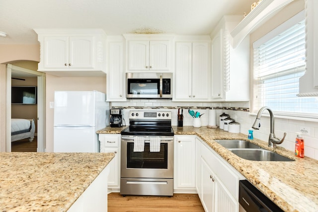 kitchen with sink, stainless steel appliances, tasteful backsplash, light stone counters, and white cabinets