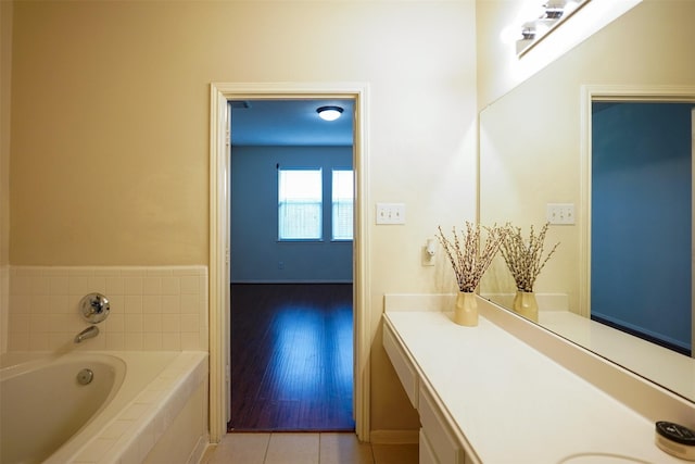 bathroom with a relaxing tiled tub, vanity, and tile patterned flooring